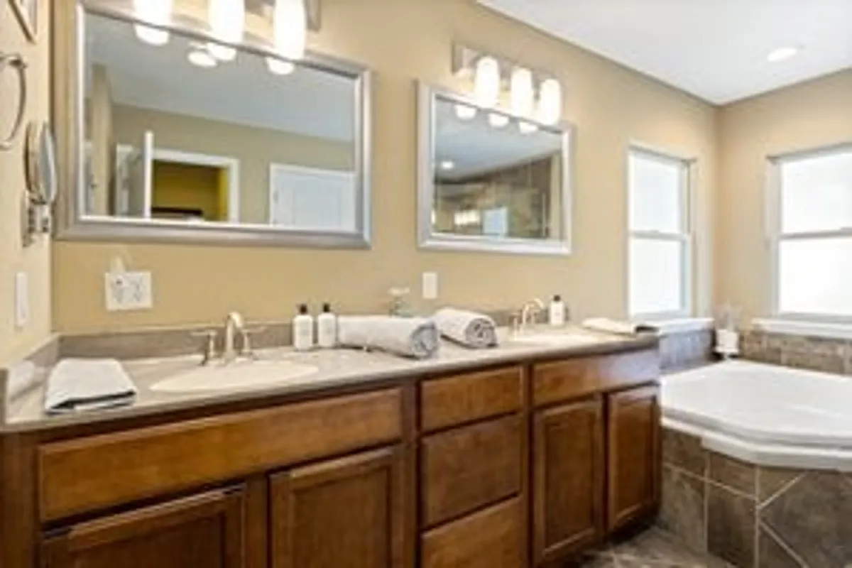 A luxurious bathroom featuring a double vanity, large mirrors, a soaking bathtub, and windows that bring in natural light. The space exudes spa-like comfort, perfect for unwinding after a day by the lake.