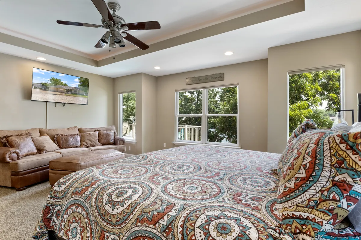 A restful bedroom with a bed dressed in patterned bedding, a small sofa at the foot, and large windows letting in abundant light. The setup offers multiple spaces to unwind, whether lounging on the sofa or enjoying the view from the bed.