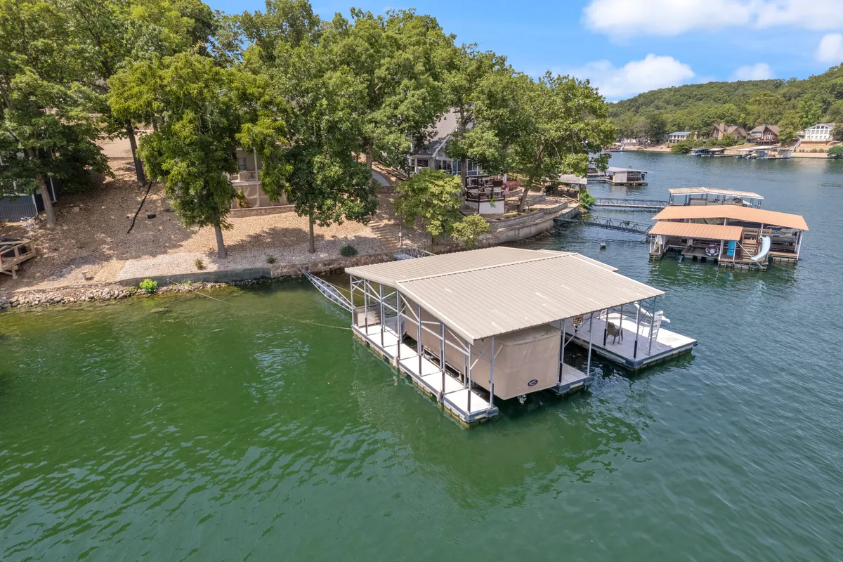 A peaceful lakeside scene featuring a boathouse and dock extending over the water, surrounded by trees and neighboring homes. The tranquil water and open sky create a rejuvenating, nature-focused atmosphere.