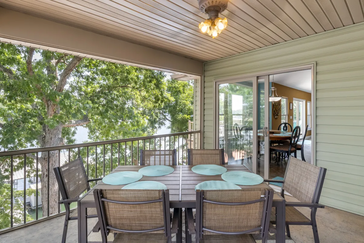 A dining table is set on a deck surrounded by green trees, with a beautiful view of the lake. The scene is peaceful, ideal for meals or gatherings outdoors while immersed in nature.