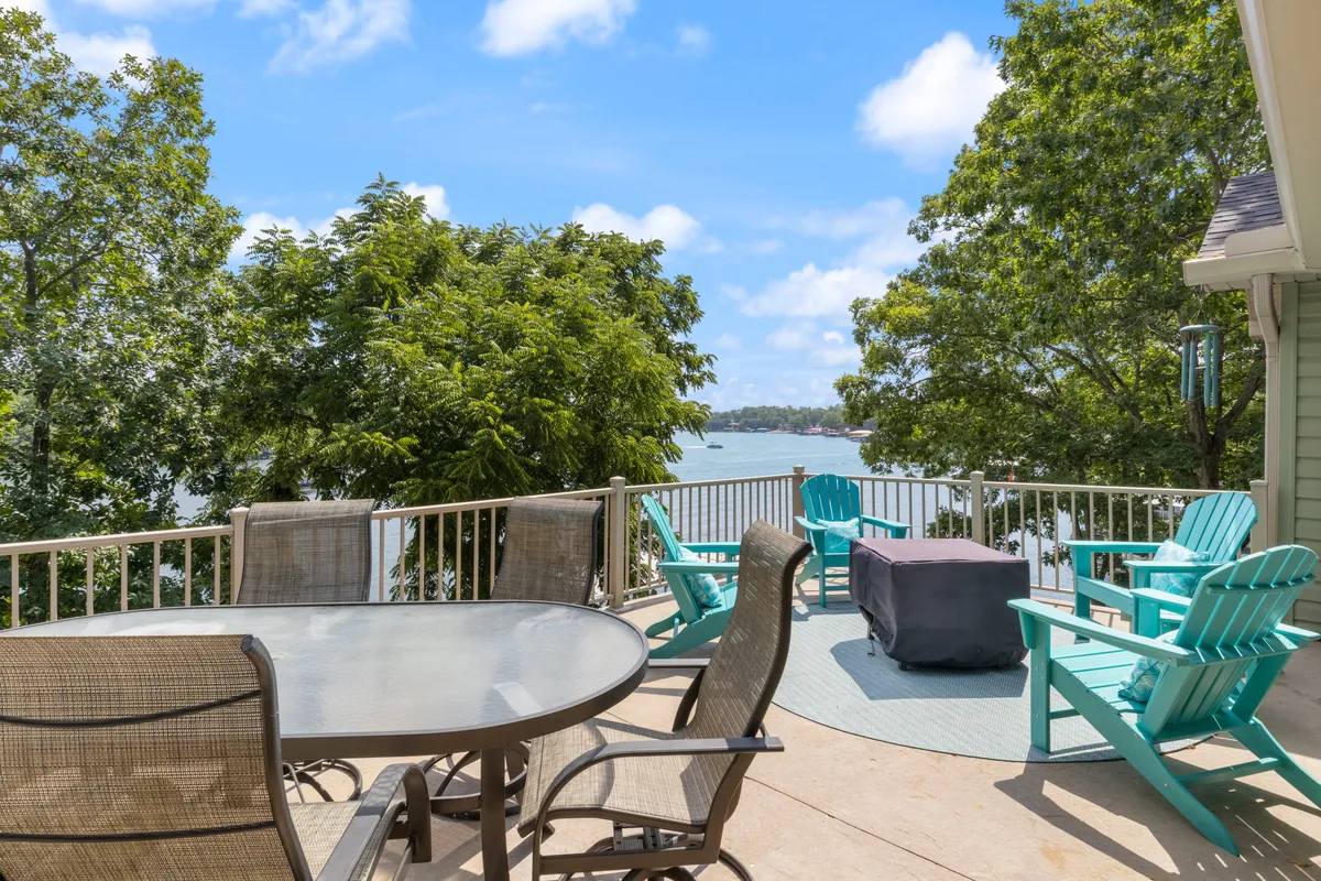 An inviting outdoor dining setup sits atop a spacious deck, with lounge chairs positioned to take in the expansive views of the water. The scene is framed by natural greenery, and the deck feels secluded, making it ideal for relaxing while observing wildlife or enjoying tranquil lake views.
