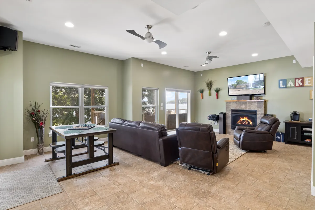 A comfortable interior space with a fireplace, plush seating area, windows framing outdoor views, and a table suitable for board games or group activities. The setting is inviting for socializing or unwinding.