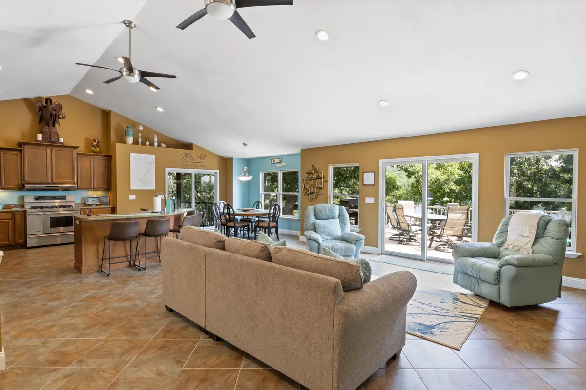 A cozy, inviting living space that blends a plush sofa with a dining table and kitchen island at the back, all illuminated by natural light streaming through large windows. The room radiates warmth and comfort, perfect for relaxing, socializing, or enjoying quiet mornings.