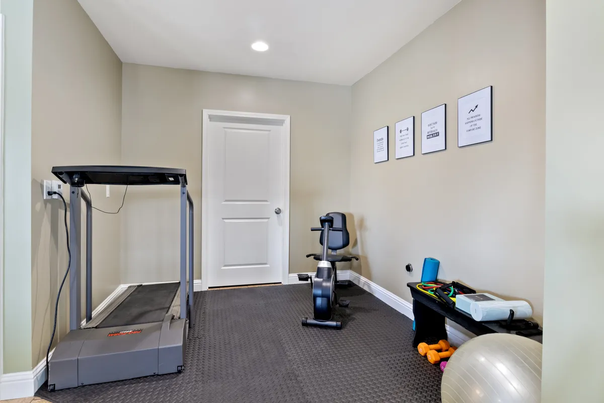 A dedicated home gym space is shown featuring a treadmill, exercise bike, yoga ball, and motivational posters on the walls. The setup includes padded flooring and open space for stretching or yoga, embodying an energetic and inspiring atmosphere.