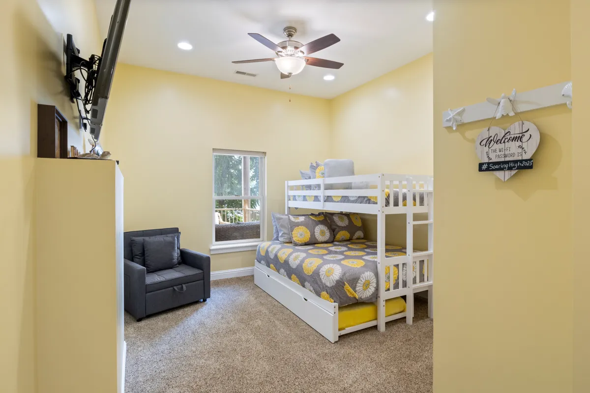 A cheerful bedroom with a bunk bed, comfortable chair, and a window offering a view. Decorated with playful accents, the room is ideal for children or families, adding a versatile option to the array of sleeping spaces.