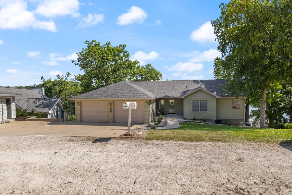 The image captures the front entrance of the home, featuring the driveway, mailbox, and mature trees. The welcoming facade is surrounded by serene greenery, suggesting a peaceful and inviting environment ideal for arrivals, outdoor relaxation, and group activities.
