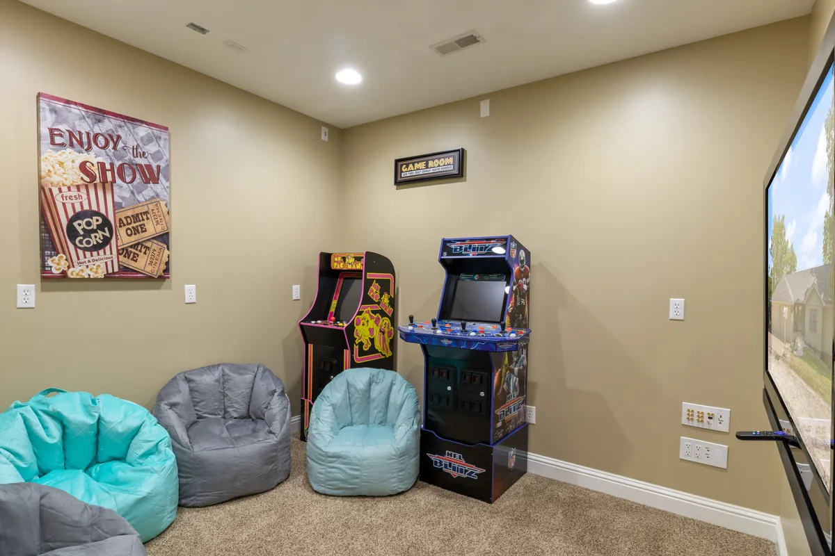 A vibrant game and movie room featuring arcade machines, cozy bean bag chairs, and playful wall art. The casual, comfortable layout invites family and friends to gather for friendly competition or relaxing movie marathons.