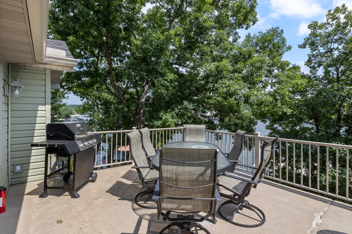 This image showcases an outdoor dining table and grill set amidst lush greenery with a water view in the background. The scene exudes a casual, inviting atmosphere perfect for outdoor meals, gatherings, and barbecues. The surrounding trees and tranquil water highlight the home's connection to nature and its potential for memorable group experiences.