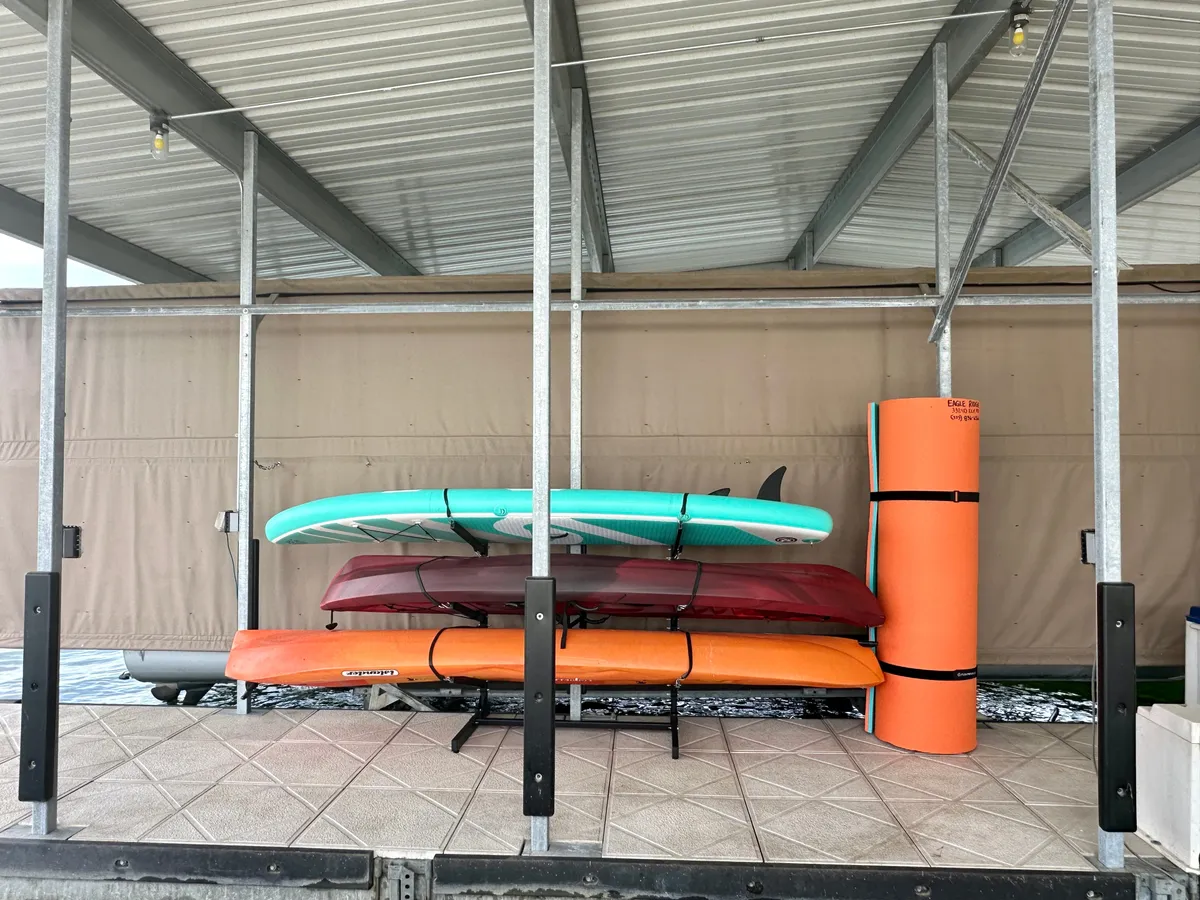 An interior storage area neatly organizes stacked paddleboards and kayaks, with bright colors and a visible foam roll creating an energetic, ready-for-action atmosphere. The scene hints at the water sports equipment available for guests’ use, suggesting easy access to active lake adventures.