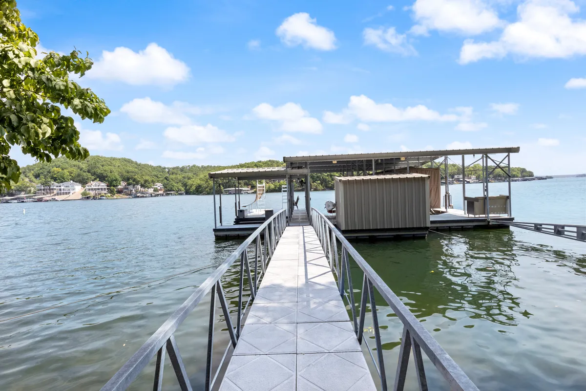 A serene boat dock extends over the calm water, surrounded by green foliage and offering a peaceful spot for fishing or relaxing. The setting sun casts a golden hue across the lake, enhancing the inviting atmosphere for water-based activities and quiet moments by the shore.