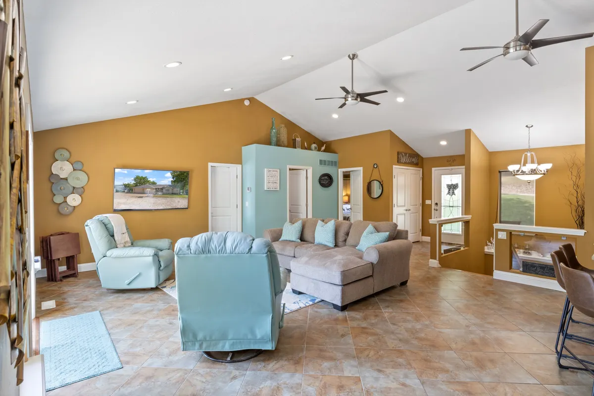 A comfortable family room featuring a large sectional sofa and a light blue recliner set around a TV with scenic landscape views. The adjacent dining area with a chandelier adds a touch of elegance, while the overall ambiance invites both movie nights and casual get-togethers.